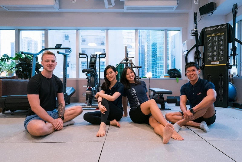 Four professional trainers sitting on the ground and smiling at Precision Fitness HK. Fitness Training Hong Kong.