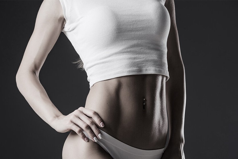Slim woman wearing white top while the focus is on her stomach